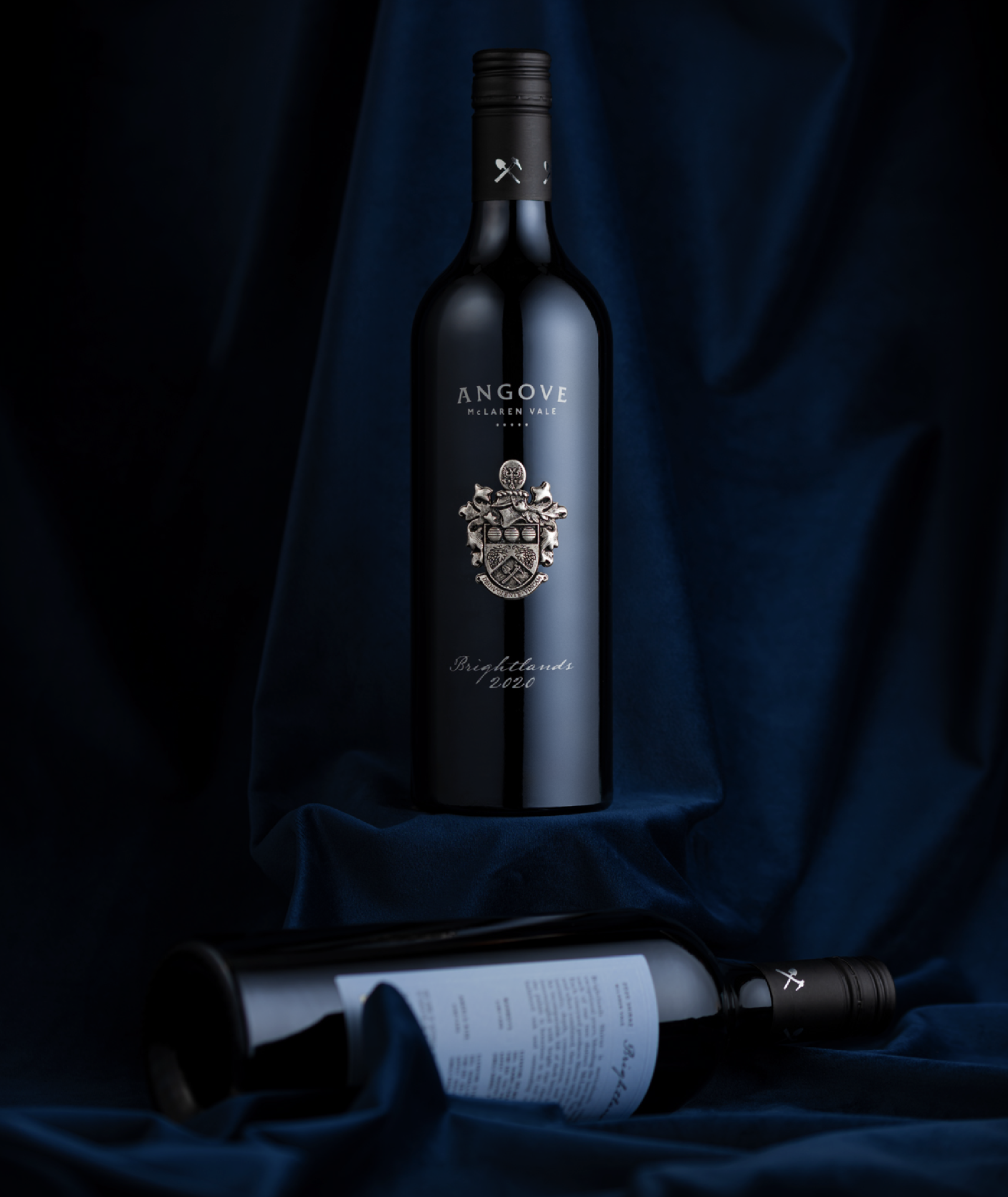 Two bottles of Angove Brightlands Shiraz on blue velvet background, one featuring the front label with the back label sitting at the bottom of the image