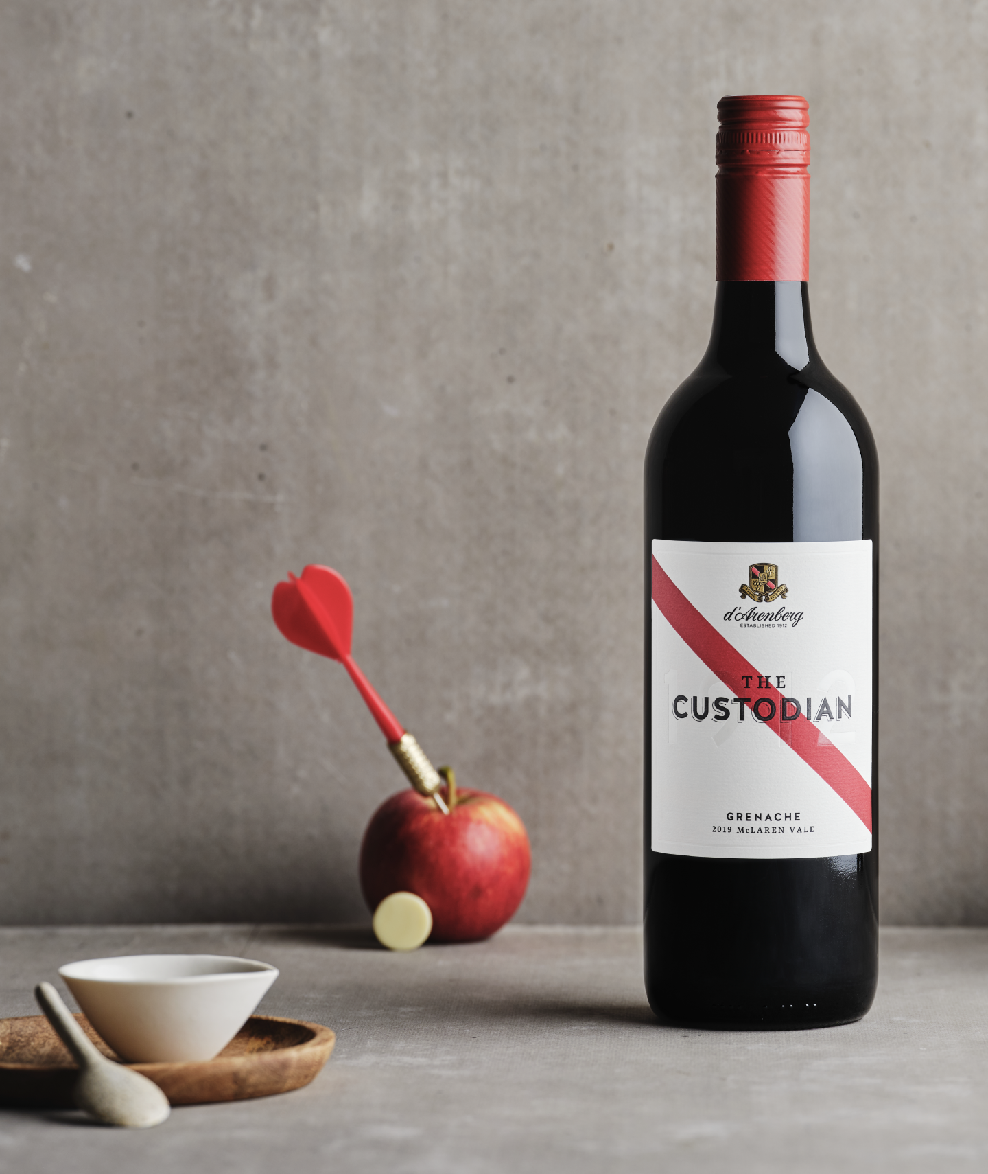 A bottle of The Custodian Grenache wine by d’Arenberg, featuring a wine label with a red stripe sitting on a table