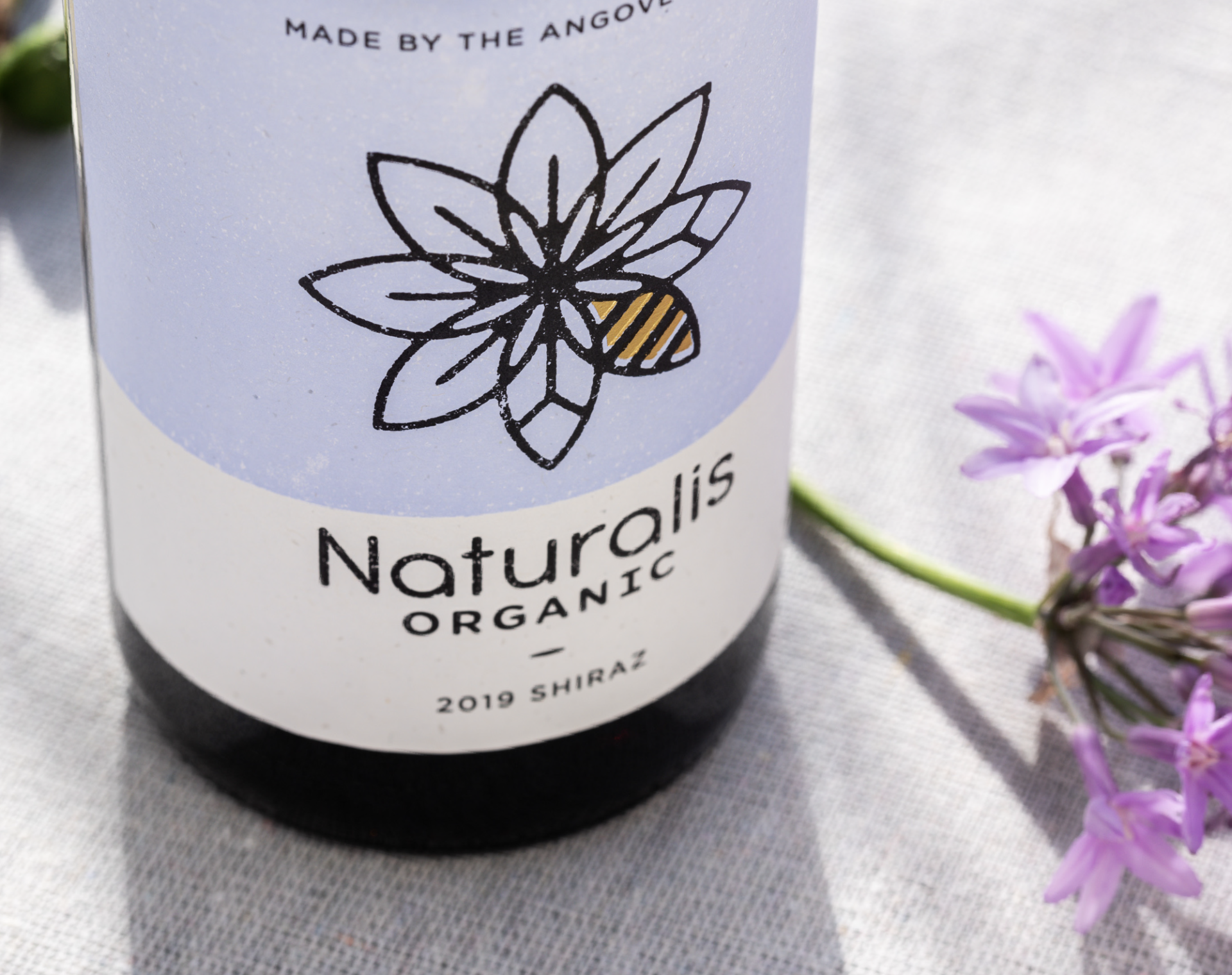 Close up of Angove's Naturalis Organic wine label showing purple Shiraz label with Naturalis flower logo and gold foil bee. 
