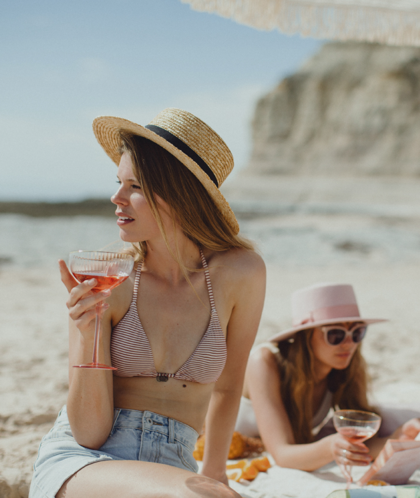 Two women on the beach in bathers and hat with a glass of Angove's Naturalis Organic wine each. 