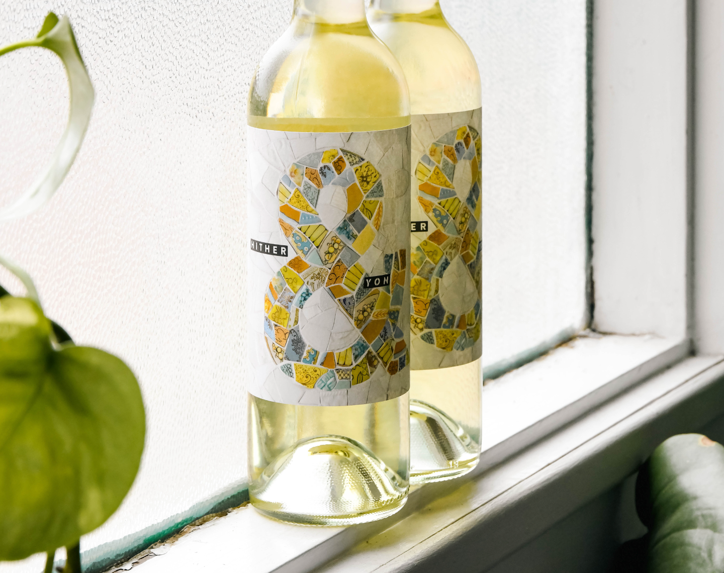 Two bottles of Hither & Yon wine sitting in a window next to a plant