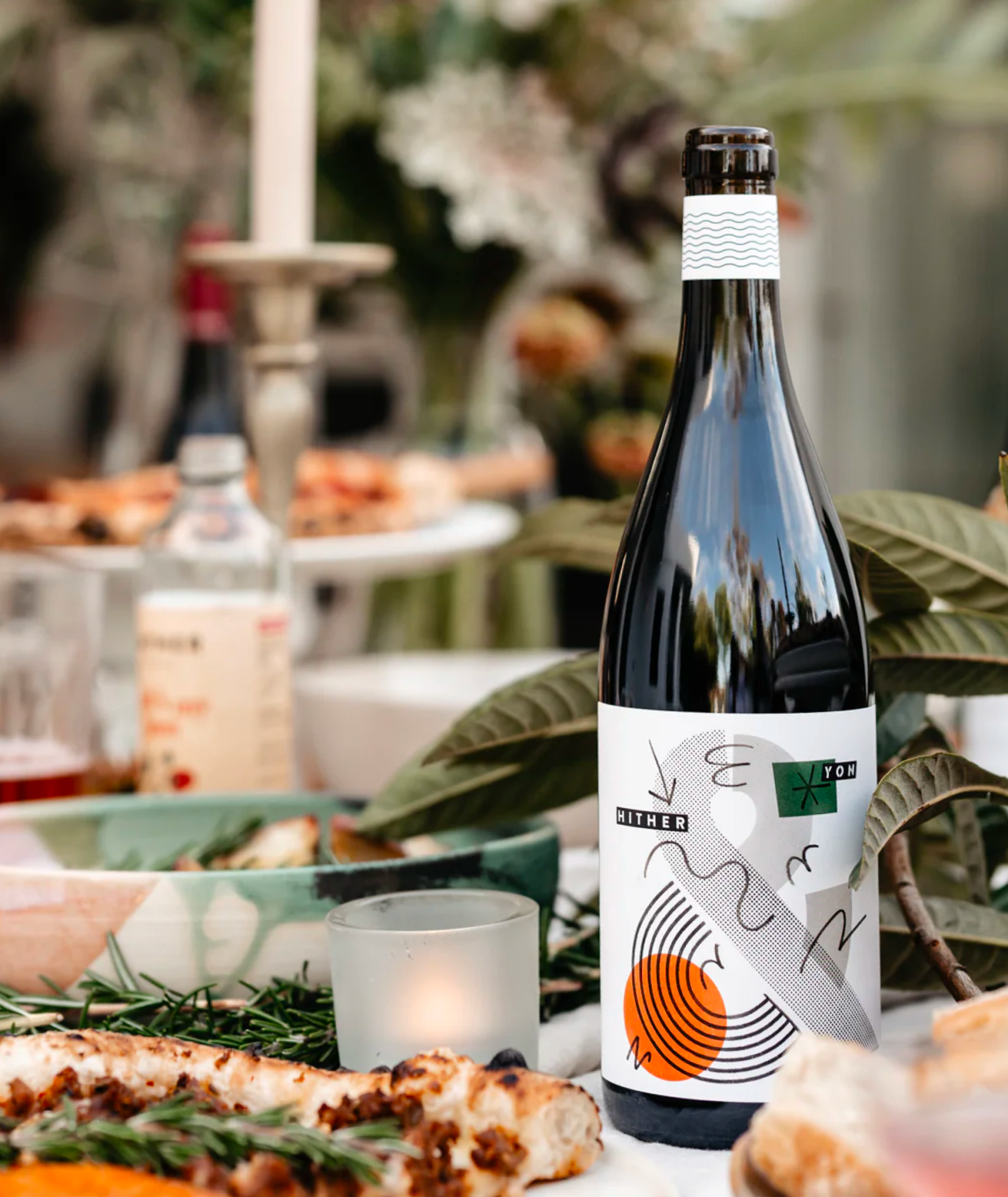 A lunch table setting with food, Hither & Yon wine and candle.
