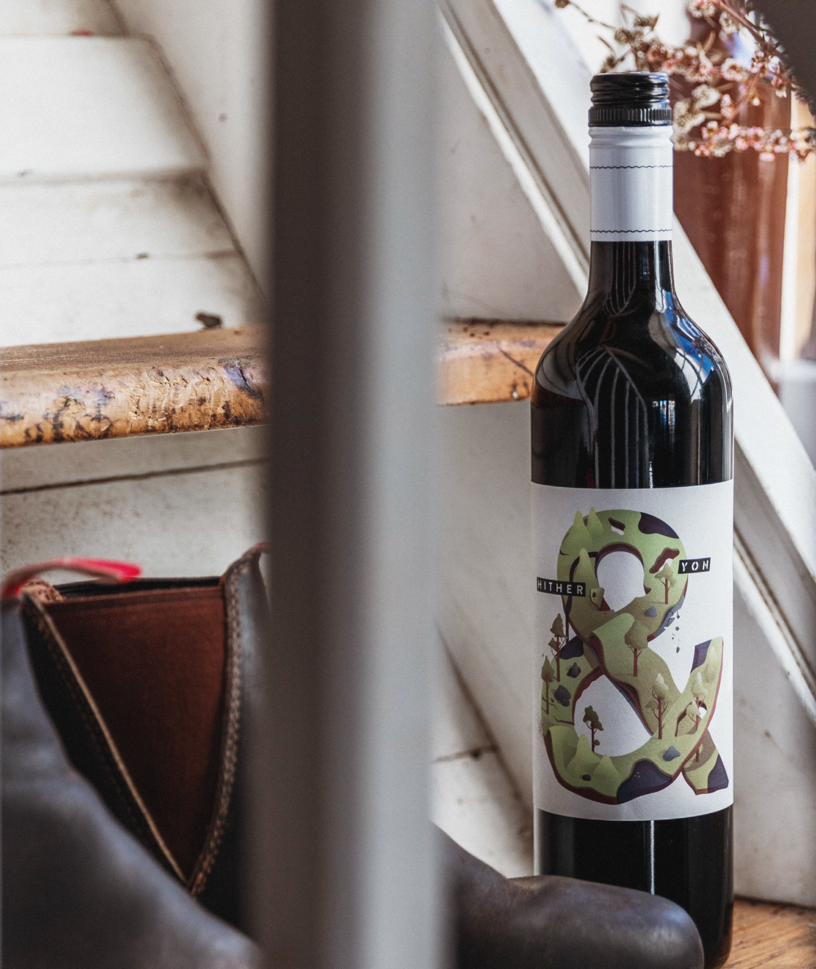 Bottle of Hither & Yon wine sitting on the floor next to a pair of boots and staircase.