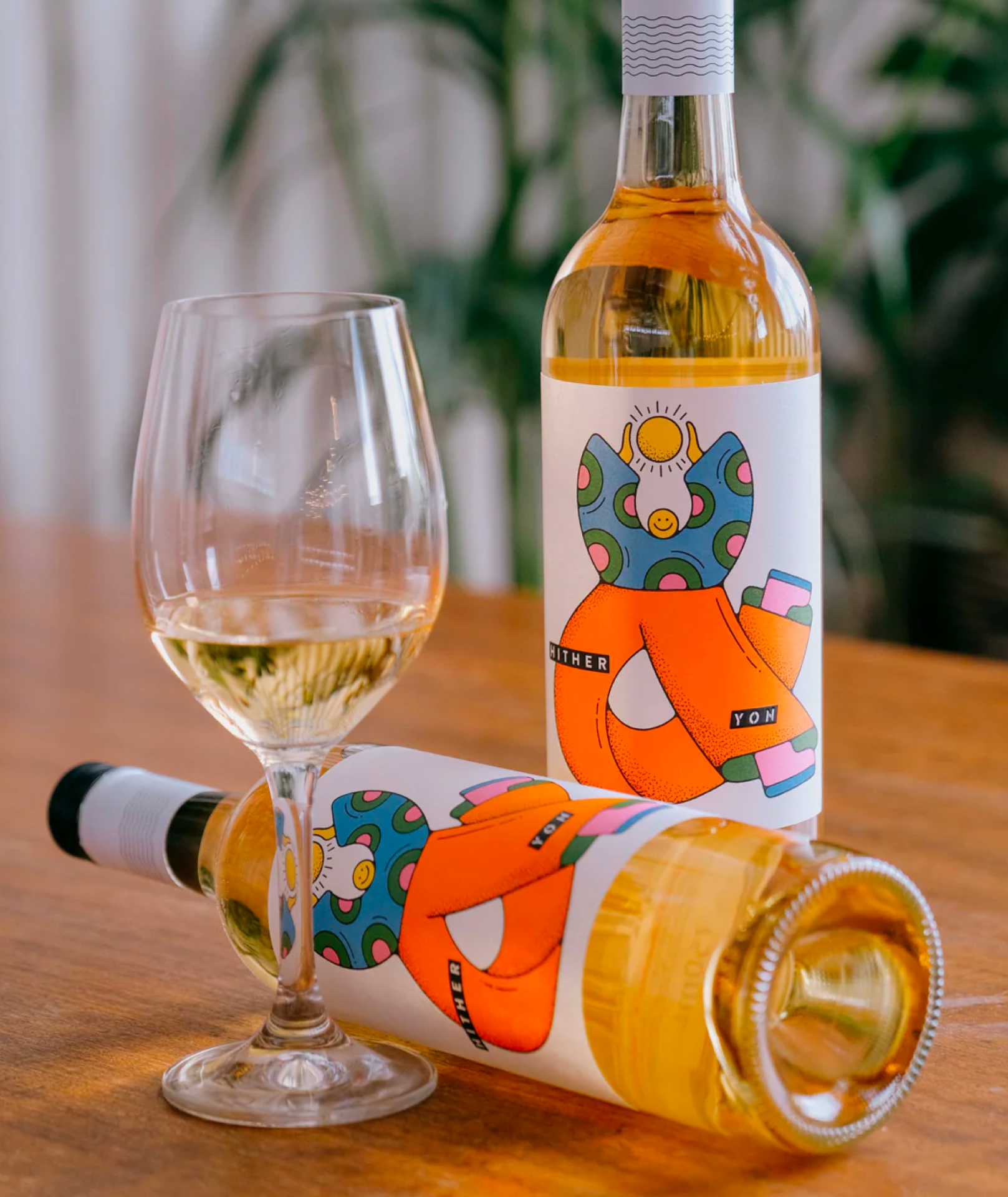 Two bottle of Hither & Yon wine sitting on a table with a glass of wine.