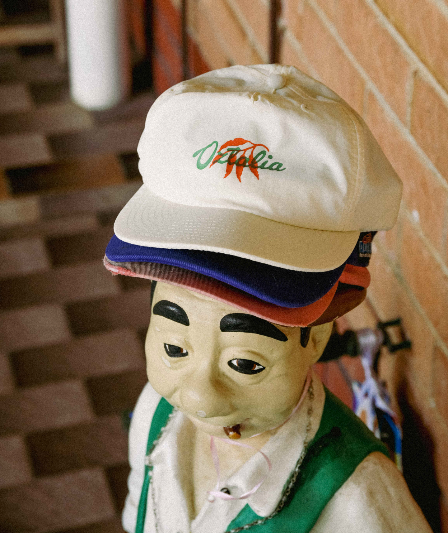 A photograph of a kitsch statue of an Italian man with an Oztalia branded hat perched on-top. 