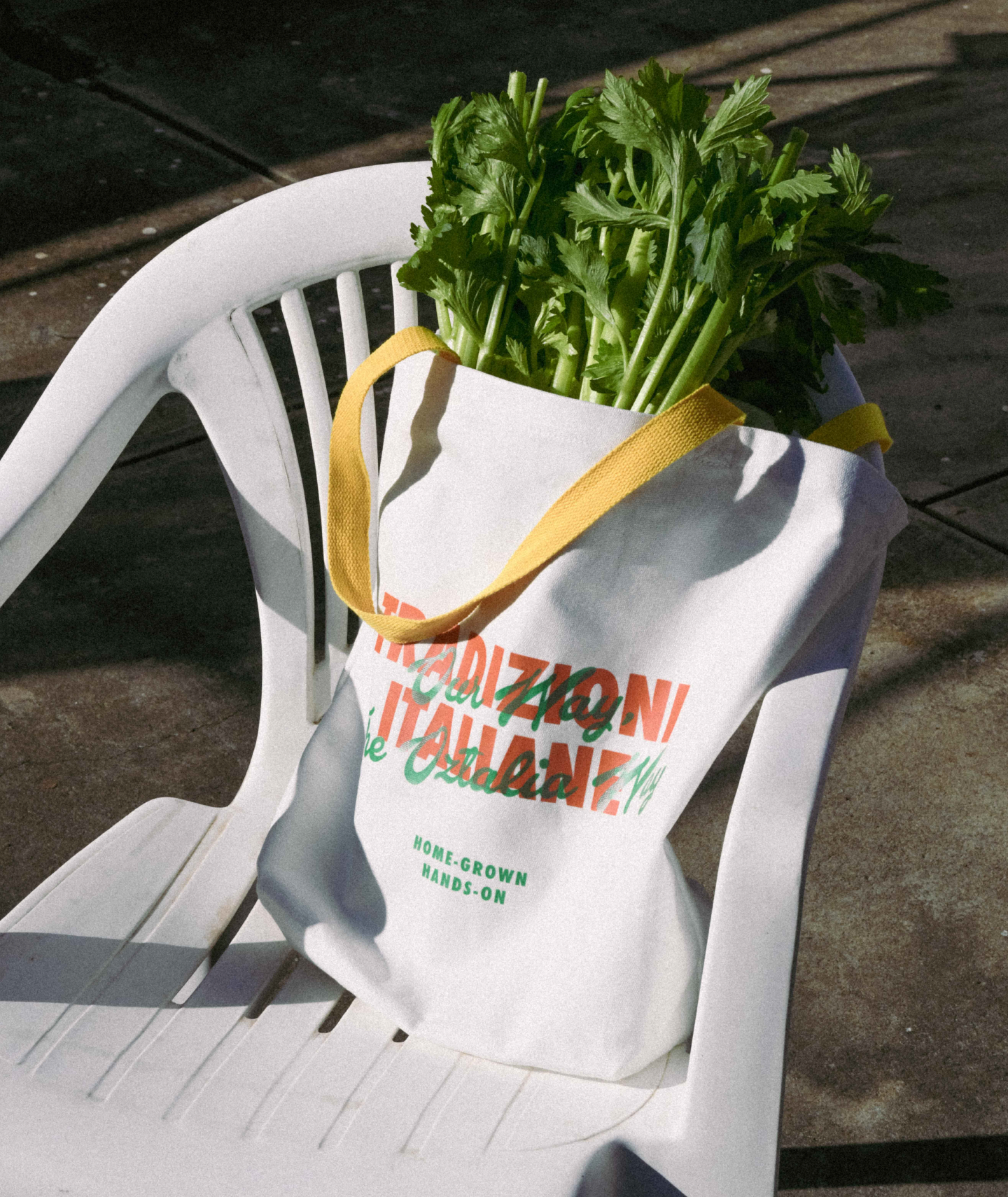 An Oztalia branded tote bag on a white plastic outdoor chair with a concrete background photographed outside. 