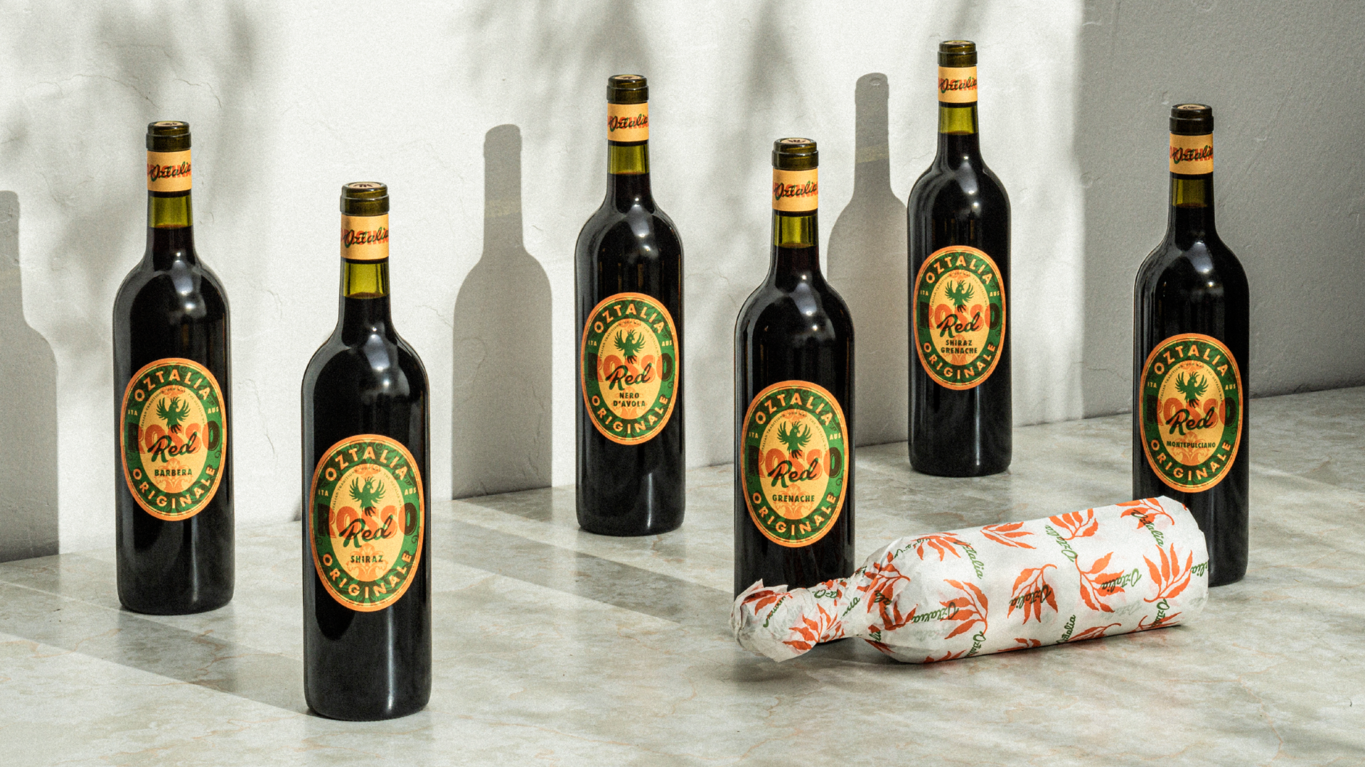 A photograph of 7 Oztalia red wine bottles on a white rendered background, showcasing their packaging and outer packaging wrap. 