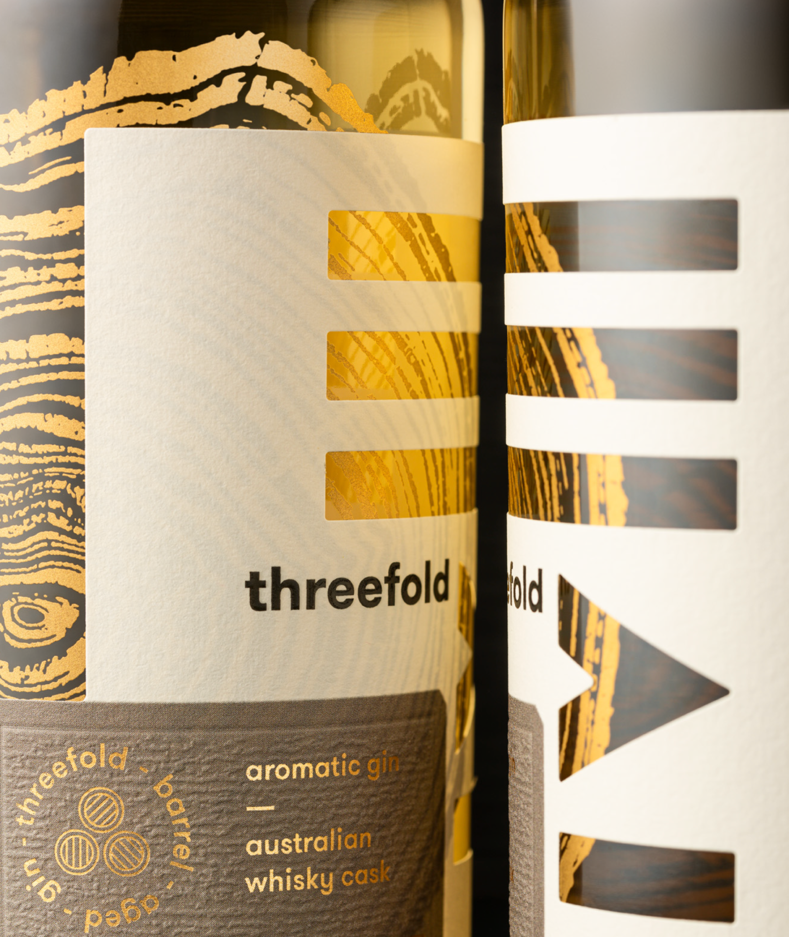 A close up of a bottle of Threefold Barrel Aged gin showing a diecut label design with gold foil over a gold screen-printed wood grain illustration.