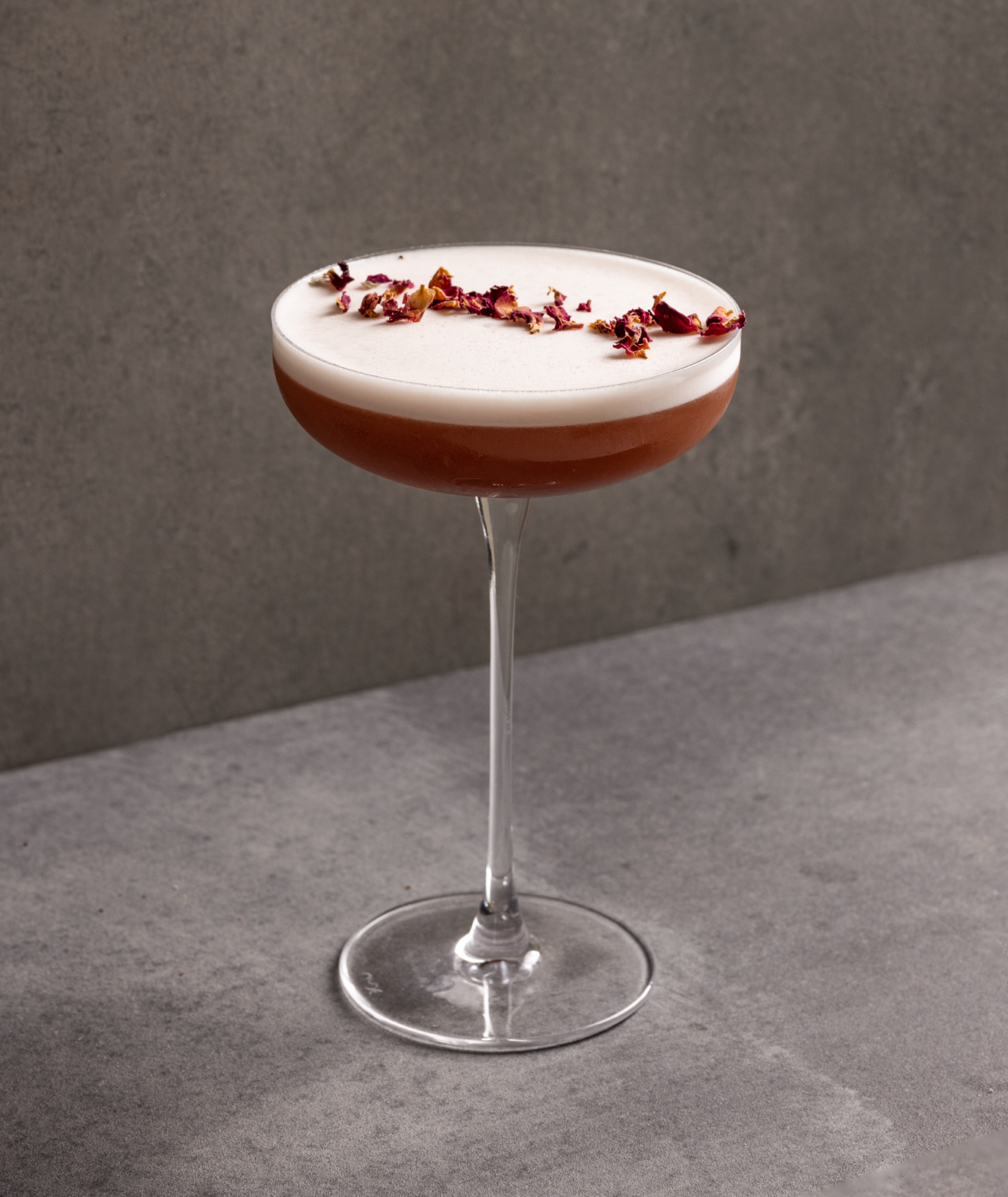 A photograph of a rose coloured cocktail in a tall coupe glass on a grey background. 