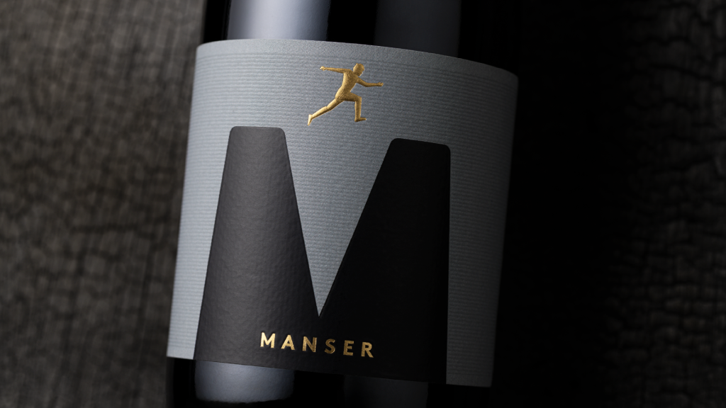 Gold sculptural emboss of a leaping figure on a dark premium wine label for the Manser Wines Estate Range, showcasing luxury wine packaging and refined label design.