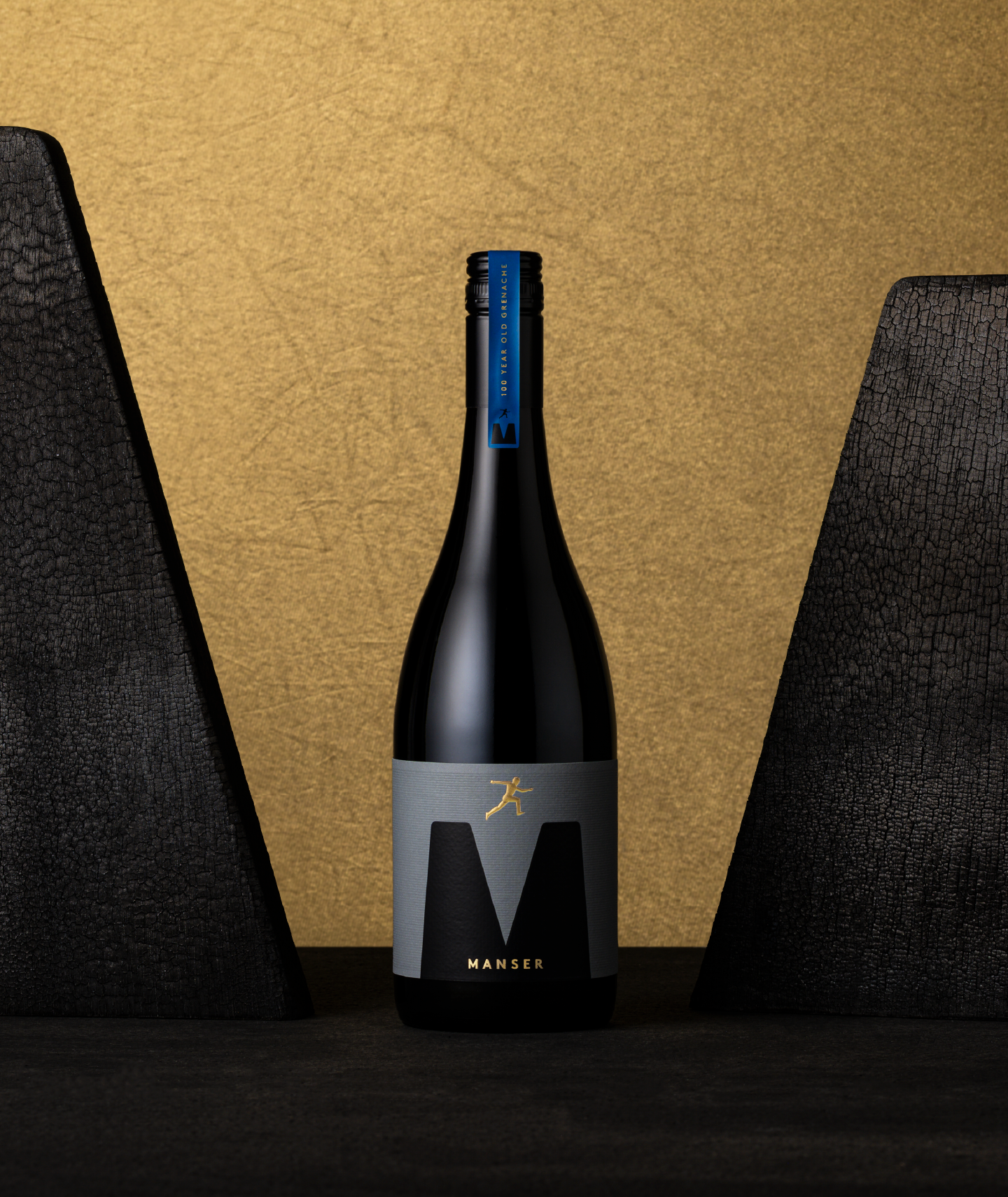 Full bottle image featuring gold sculptural emboss of a leaping figure on a dark premium wine label for the Manser Wines Estate Range, showcasing luxury wine packaging and refined label design.