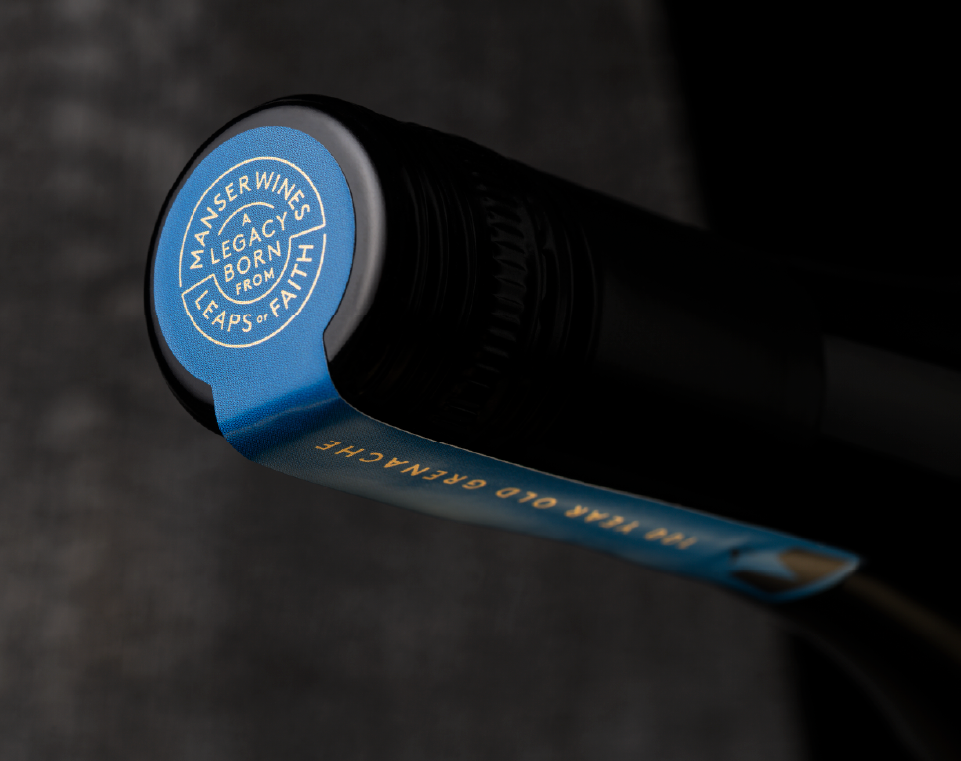 Wine bottle with an over-label sticker featuring gold foil, presenting a premium roundel with the brand positioning: “Manser Wines, A legacy born from leaps of faith.”