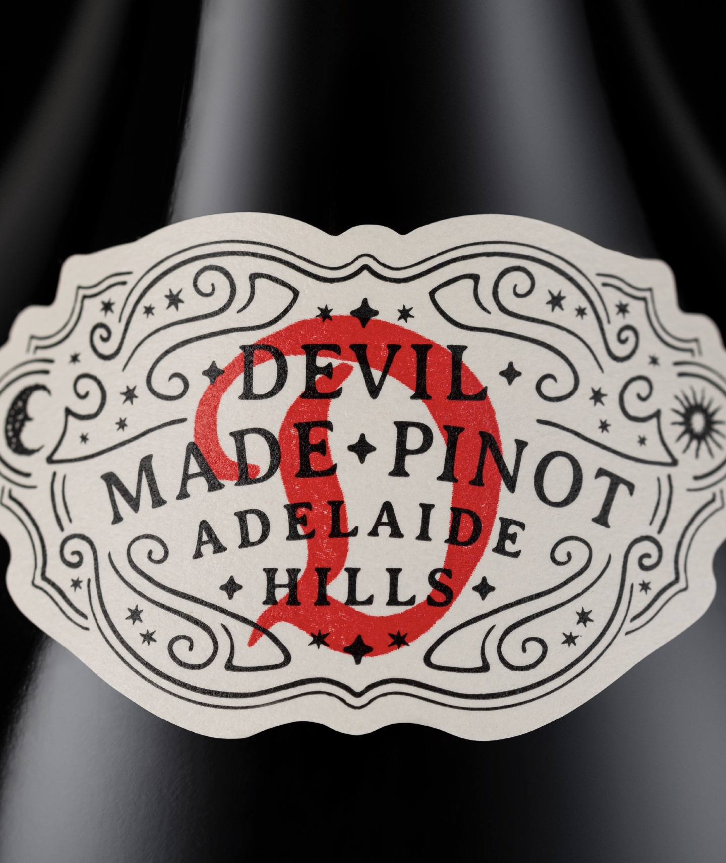 Shoulder label design for The Devil Made Pinot, featuring a custom ornate monogram, devil branding, and celestial motifs printed on premium textured paper stock.