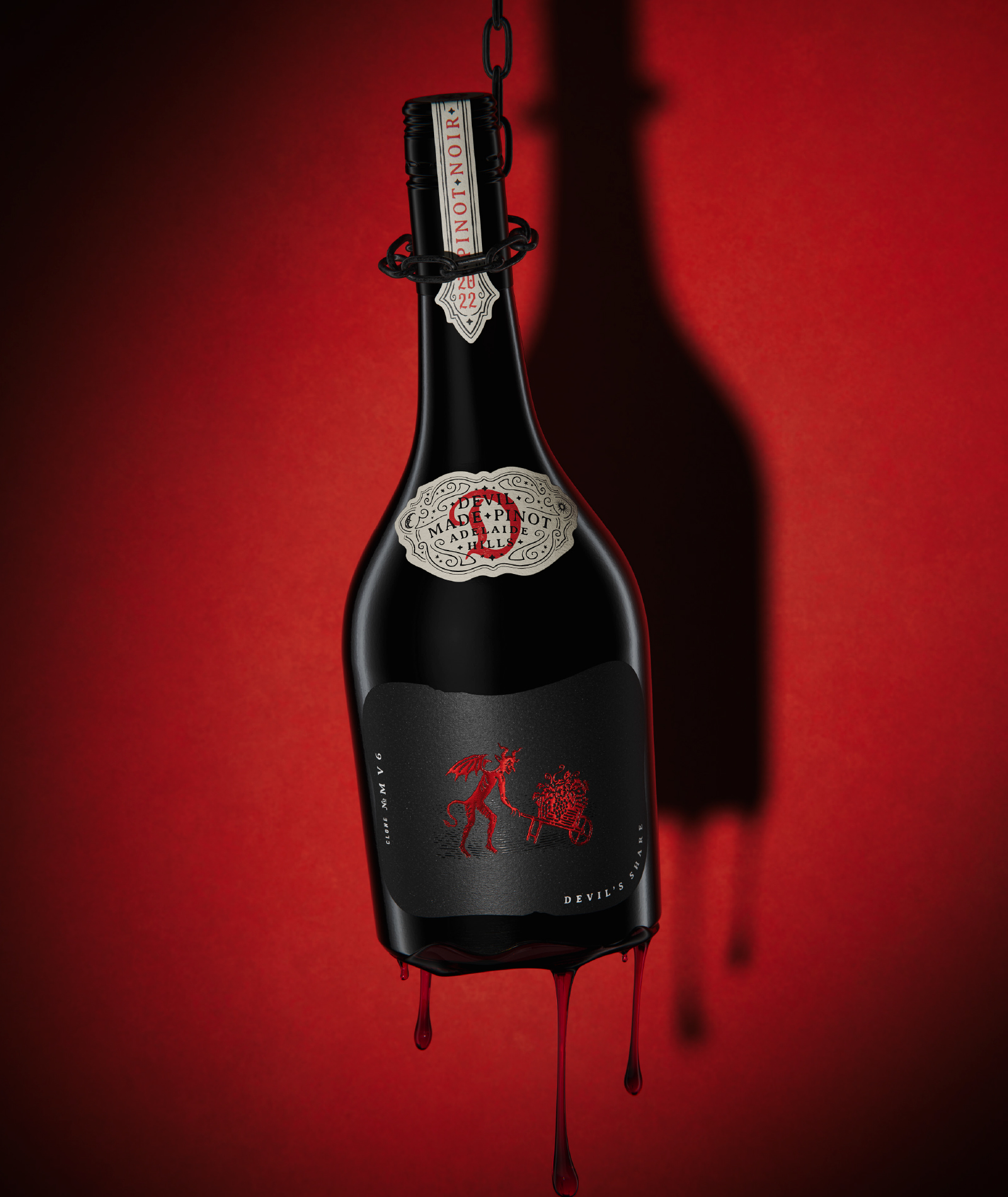 Premium wine packaging for The Devil Made Pinot Single Clone 'Devil's Share' variant, featuring a hanging bottle, dark matte label, and signature devil illustration